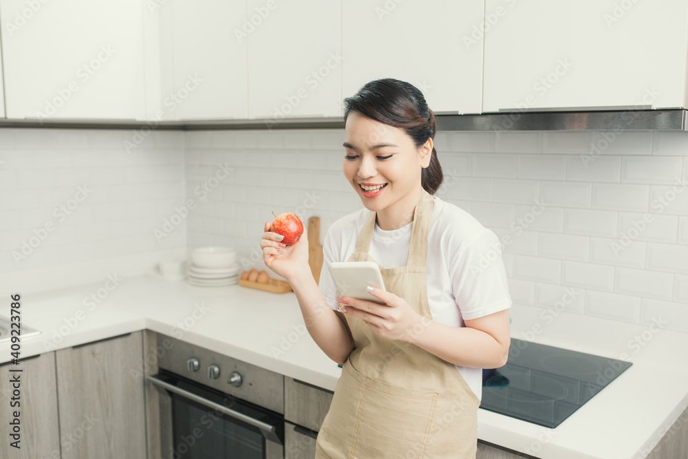pretty young woman using her mobile phone while eating an apple in the kitchen at home. pretty young woman using her mobile phone while eating an apple in the kitchen at home.