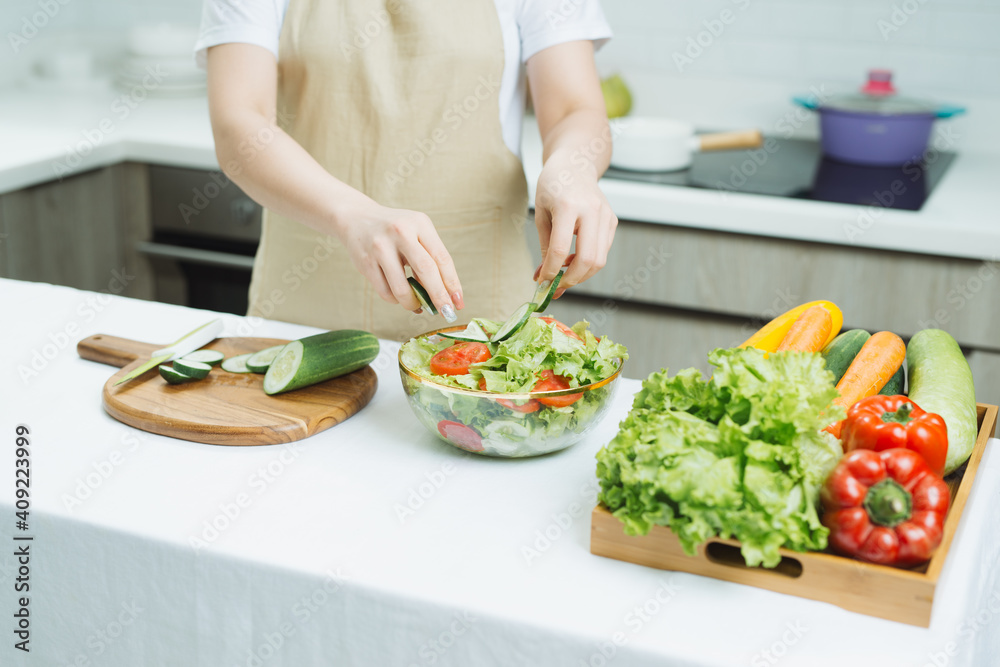 Smiling young woman in apron stand in modern kitchen preparing salad