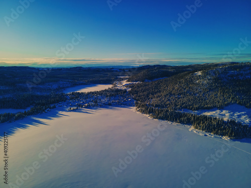 Frozen lake in the Norwegian wilderness  covered in undisturbed snow on a bright sunny day. Aerial photo.