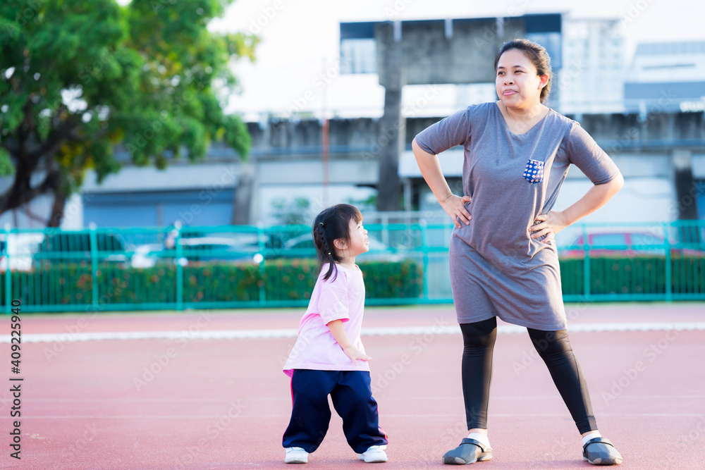 Mother and daughter are exercising. Cute girl laughed happily and looked at her mom. The mother made a irksome face be merciful for the little child. The family enjoyed the evening sport activities.