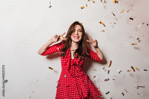 Portrait of positive lady laughing against background of confetti. Brunette has fun at party and shows signs of peace