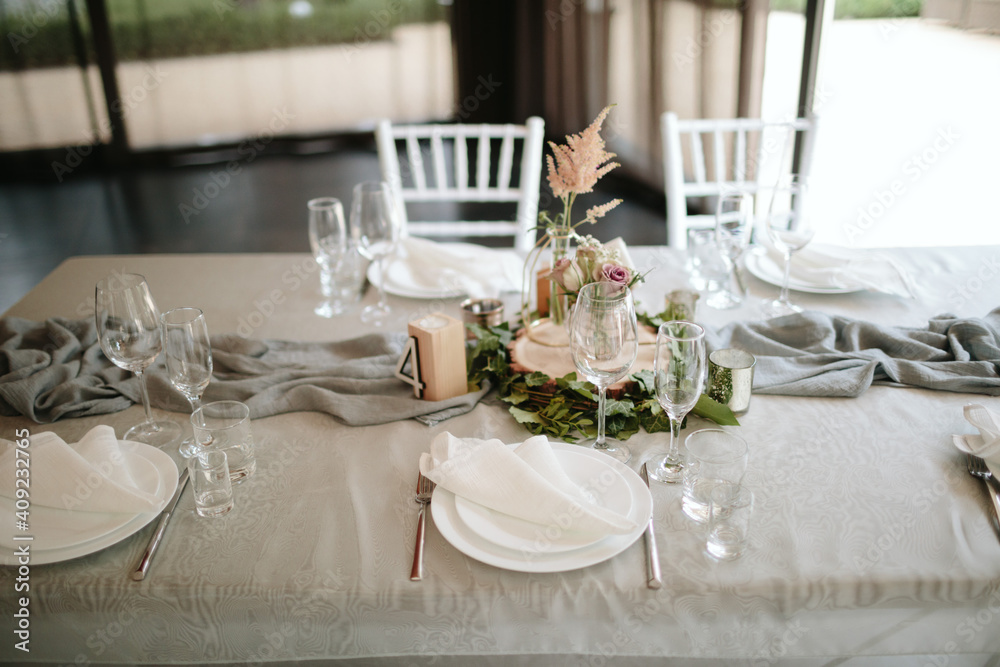 Vintage wedding decor. Beautiful event venue. Creative decoration. Hall decoration. Festive table decor. Stylish stone tablet with table number in grey, green branches and peonies, candles in gold can