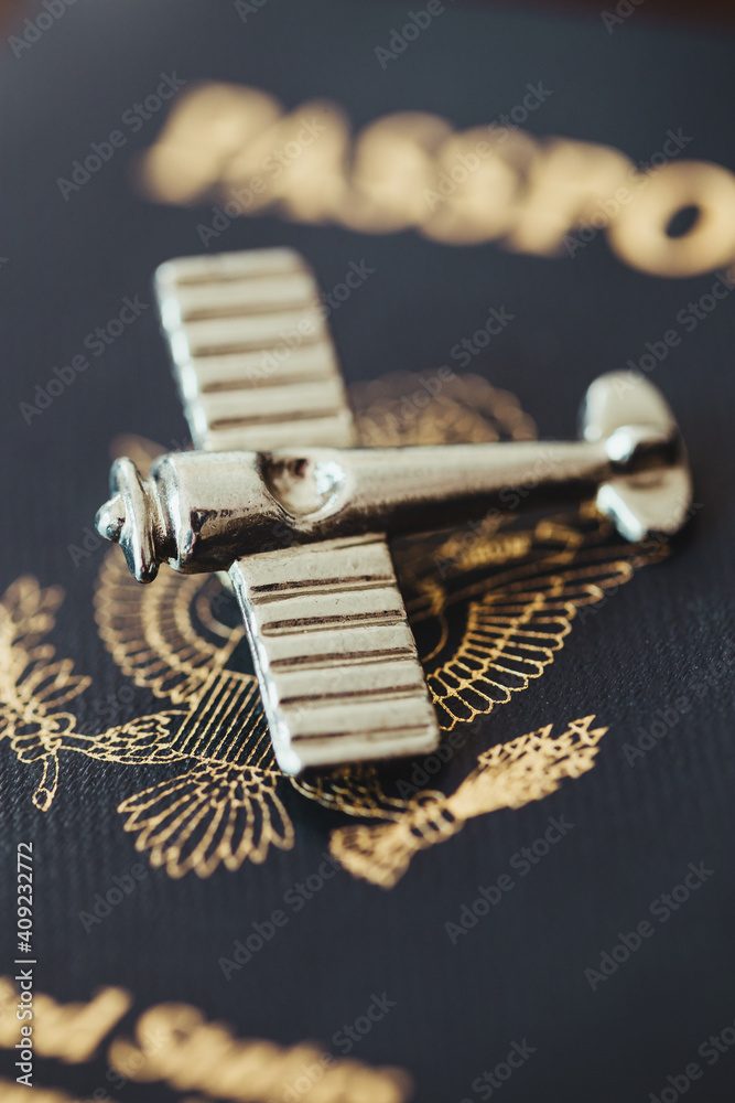 A silver antique airplane sitting on top of a blue American passport A silver antique airplane sitting on top of a blue American passport