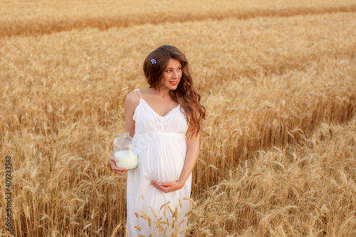 a pregnant woman with a can of milk walks in a wheat field