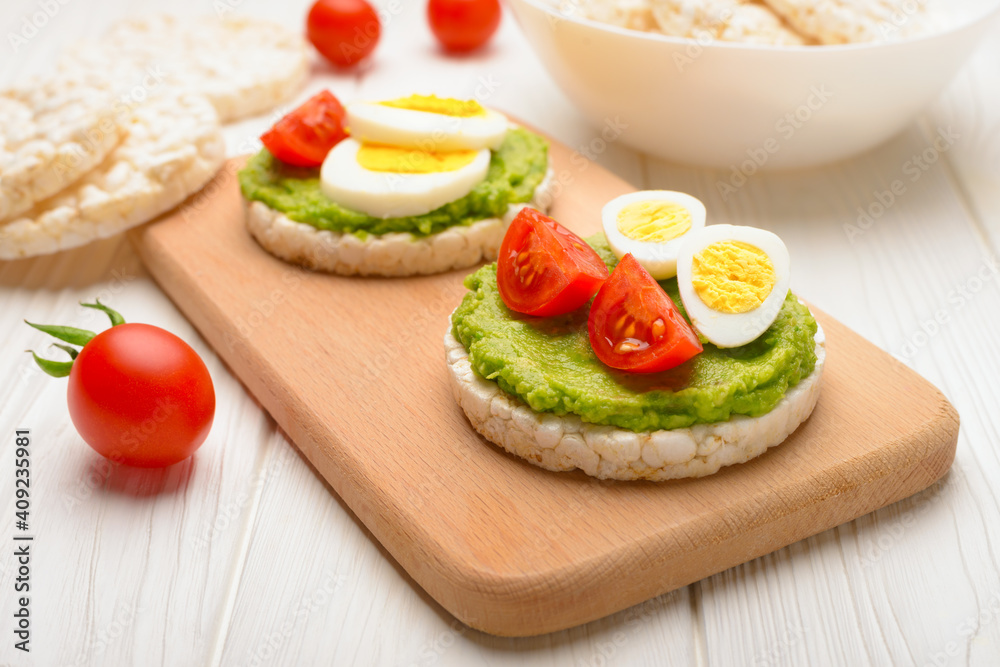 Rice cakes with avocado mash and eggs with tomato on cutting board