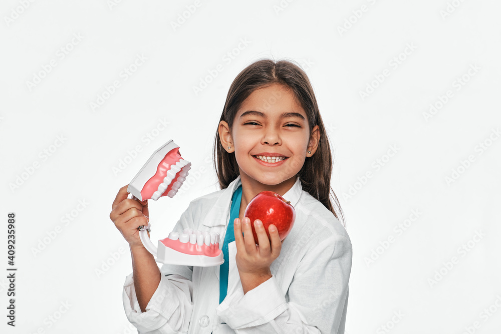 Latino Americano child with a toothy smile, holding a model of jaw and apple in her hands. Fruits are very healthy for children's teeth Latino Americano child with a toothy smile, holding a model of jaw and apple in her hands. Fruits are very healthy for children's teeth