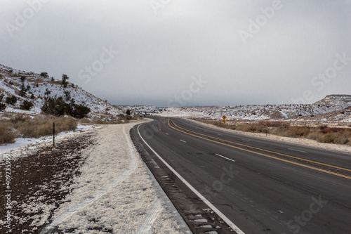 Empty highway cutting through snow covered valley in rural New Mexico on overcast day