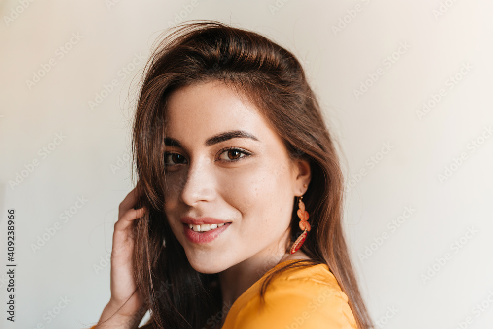 Close-up shot of young beautiful girl with brown eyes. Lady in bright earrings and yellow top smiles sweetly Close-up shot of young beautiful girl with brown eyes. Lady in bright earrings and yellow top smiles sweetly