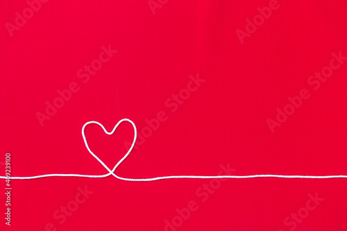 White cotton thread in heart shape on red fabric background, love and romance concept, valentine background idea