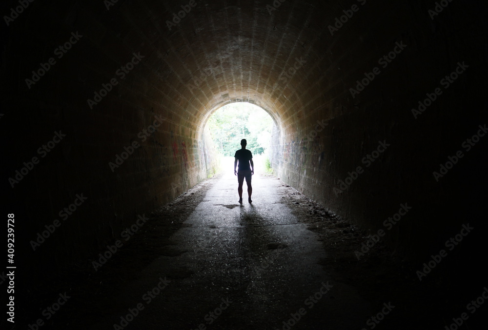 Escape the Darkness - silhouette of man standing in the light at the end of the tunnel