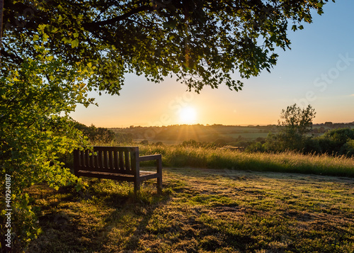 Canvas Print Lone bench seat overlooking countryside view with sunset orange sky nature reser