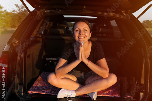 happy beautiful girl sitting in the trunk of car and enjoying sunset on the roadside. young woman in the car