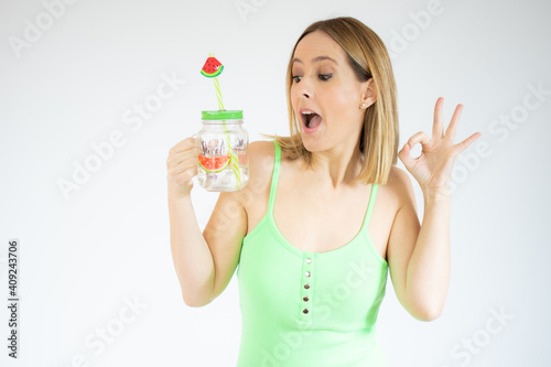 Happy young woman holding cold drink showing okay sign with fingers isolated over white background
