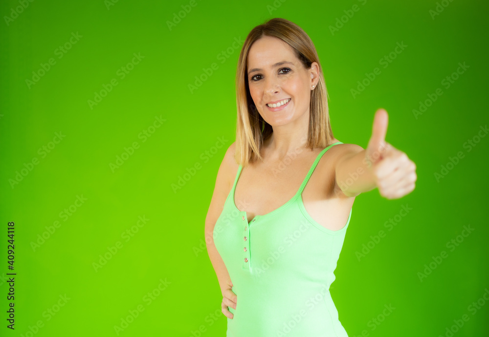 Young happy cheerful woman showing thumb up over green background. Young happy cheerful woman showing thumb up over green background.