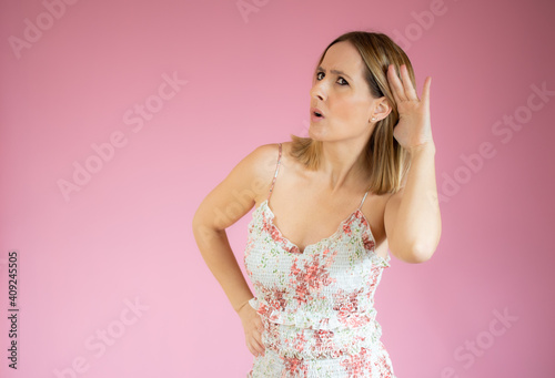 Young woman over isolated pink background listening to something by putting hand on the ear © Danko