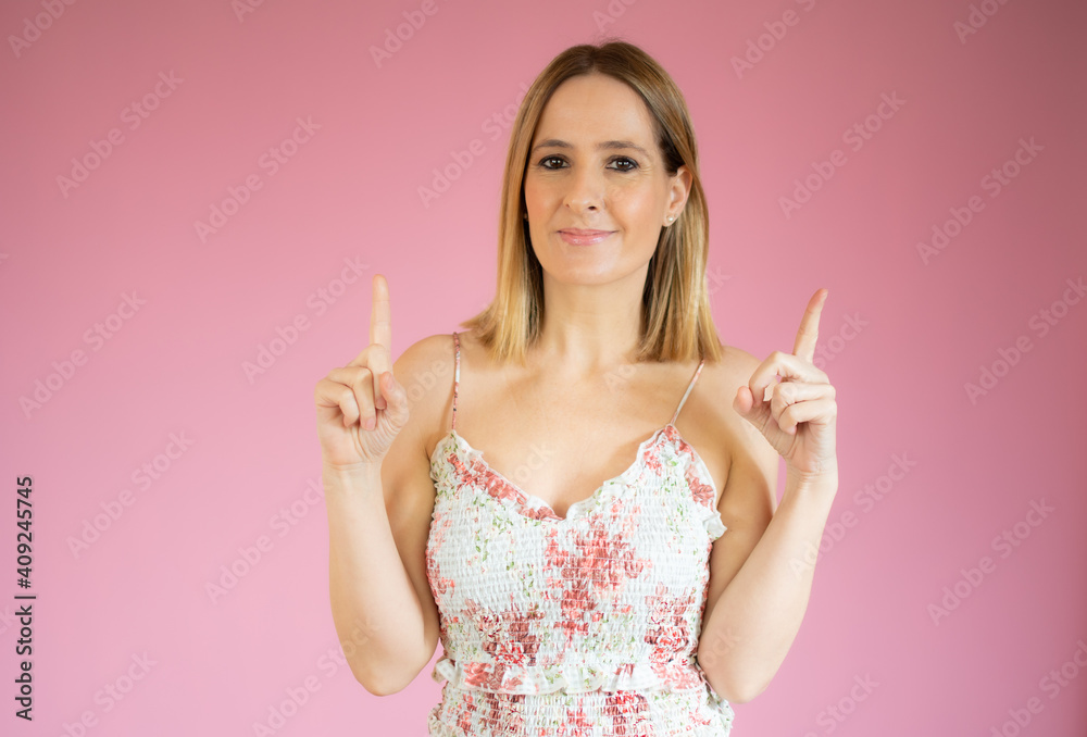 Portrait of a happy young woman dressed in casual dress pointing fingers up at copy space isolated over pink background Portrait of a happy young woman dressed in casual dress pointing fingers up at copy space isolated over pink background