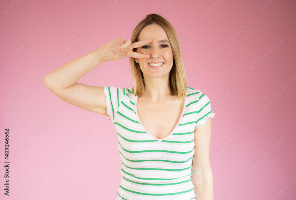 Portrait of a smiling happy woman showing victory sign and looking at camera isolated over pink background Portrait of a smiling happy woman showing victory sign and looking at camera isolated over pink background
