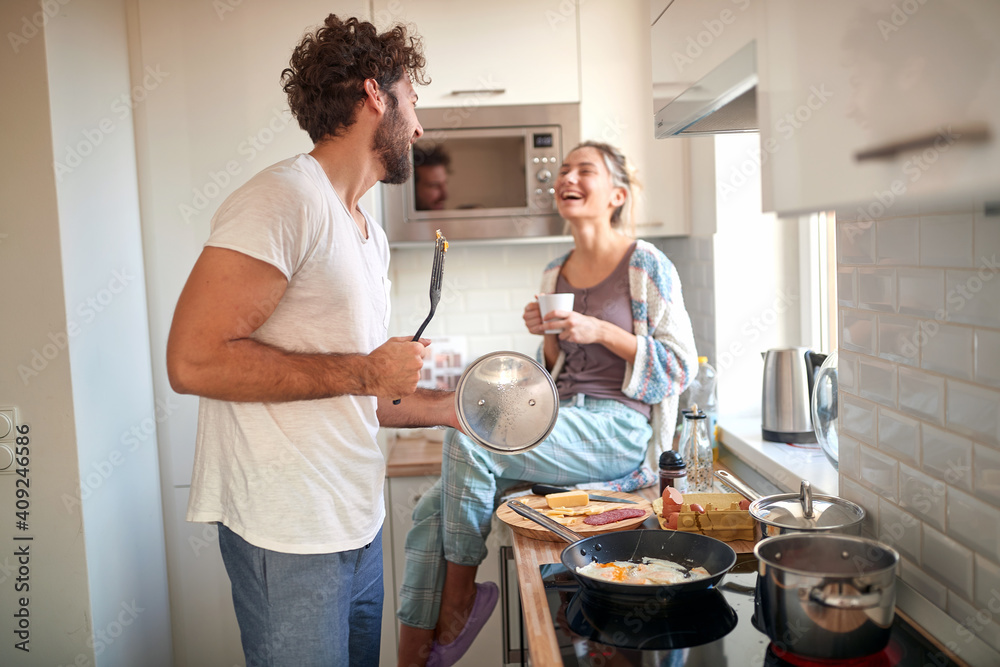 A young couple in love having fun while preparing a breakfast together. Cooking, together, kitchen, relationship - obrazy, fototapety, plakaty 