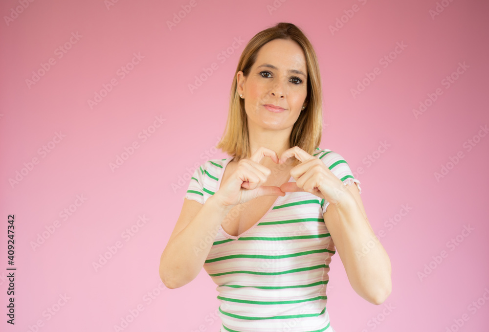Young woman in striped t-shirt making heart figure over pink background. Young woman in striped t-shirt making heart figure over pink background.