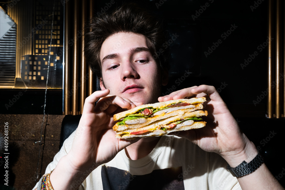 young man holding a sandwich in his hands. young man holding a sandwich in his hands.