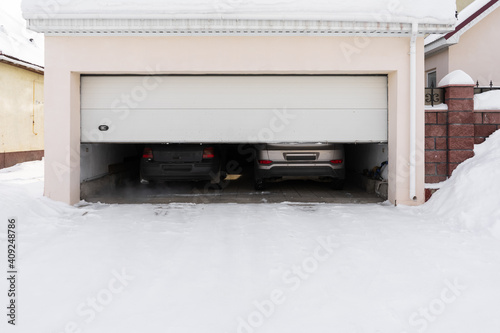 xterior of a garage attached to a house. garage with two cars inside in winter. semi-open sectional doors photo