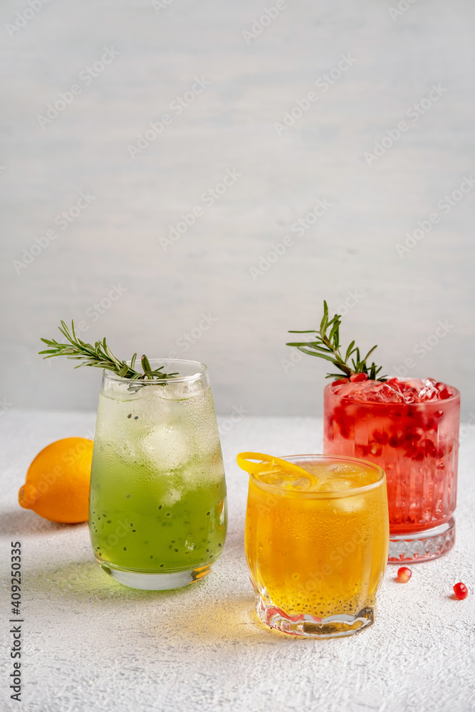Fototapeta premium Three colorful summer cocktails in glasses on white table. Assortment of fresh summer drinks. Red sangria cocktails, orange punch cocktail, margarita cocktail, tropical mule.