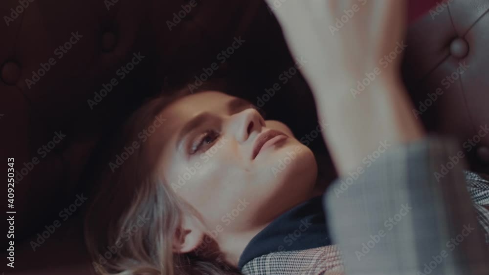 Young attractive caucasian woman holds a book in her hands and reads it while lying on the couch in the library and smiles a little Young attractive caucasian woman holds a book in her hands and reads it while lying on the couch in the library and smiles a little