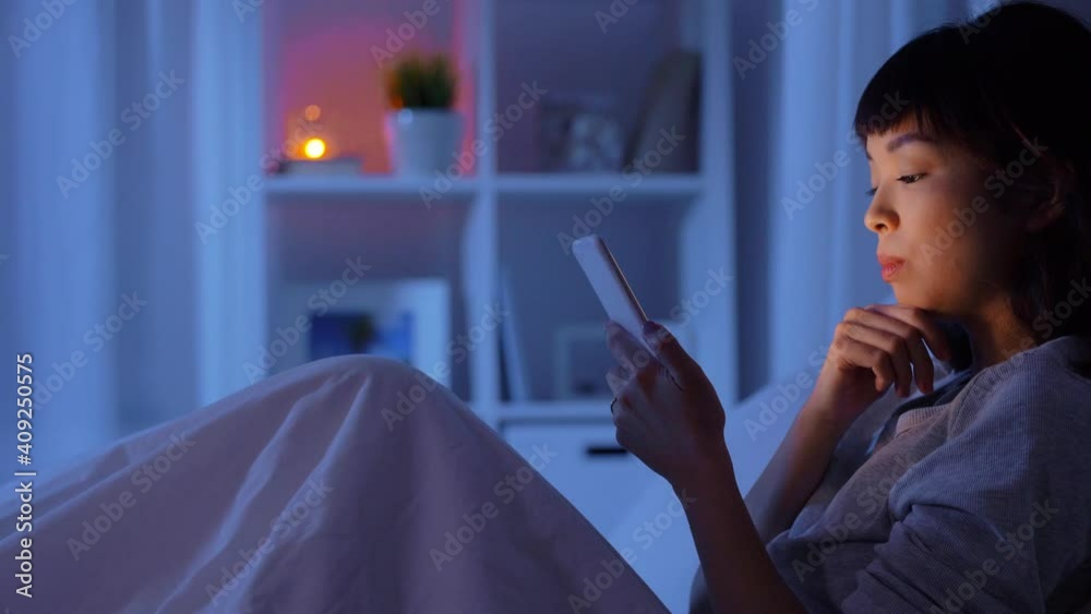 technology, internet and people concept - young asian woman with smartphone lying in bed at home at night