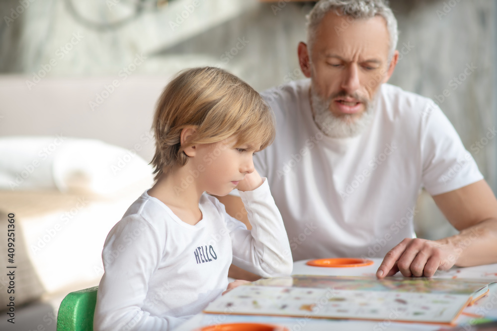 Boy reading a book together with his grandfather Boy reading a book together with his grandfather