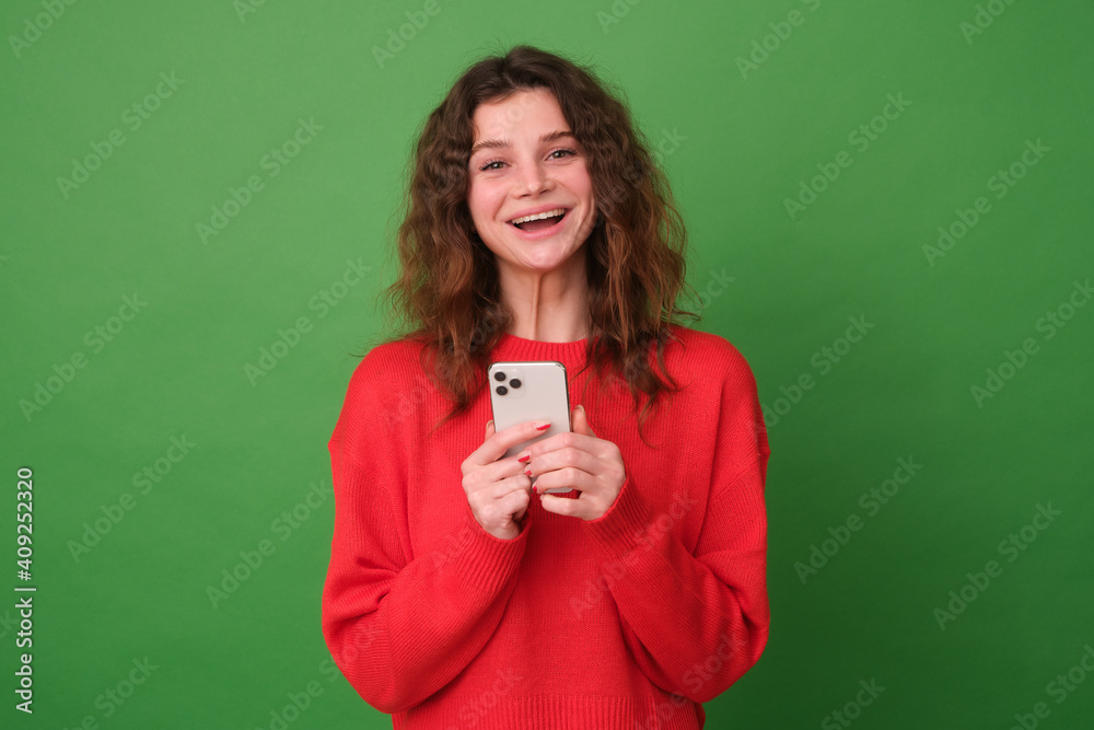 Beautiful young girl in red clothes on a green background. The girl laughs at the camera from the received message. The concept of emotions Beautiful young girl in red clothes on a green background. The girl laughs at the camera from the received message. The concept of emotions