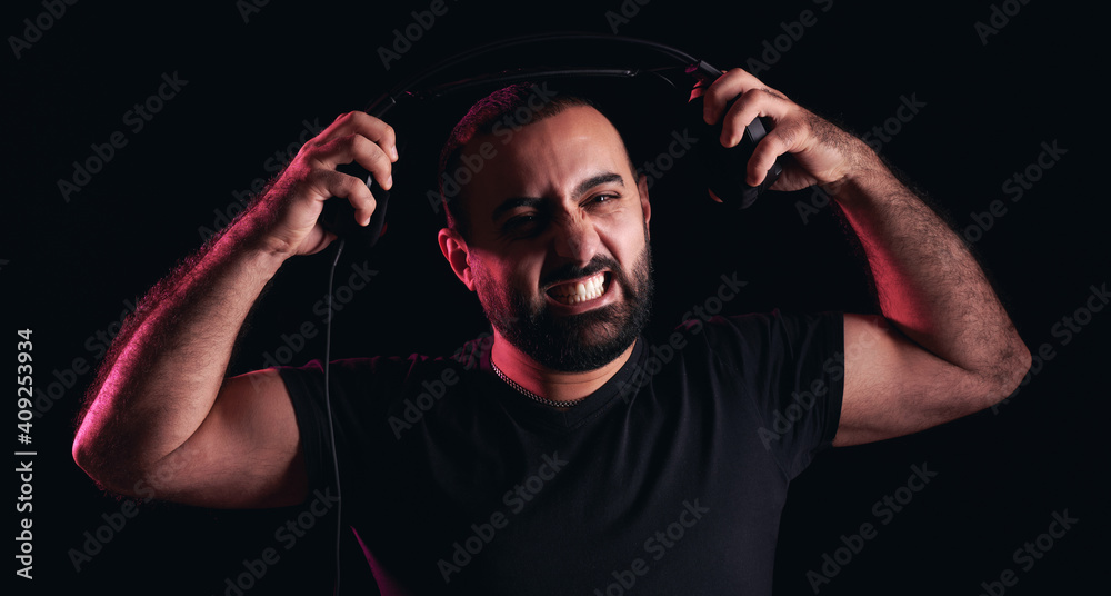 Angry screaming bearded arabic musician dj tearing headphones on black isolated background. International DJ Day
