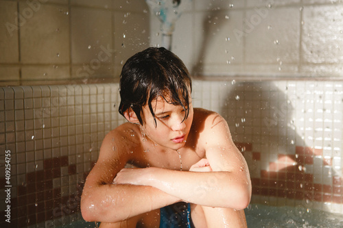 A beautiful boy sits in a pool with water drops falling around him photo