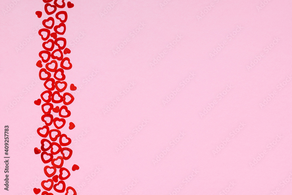 Top view of vertical strip of small heart shaped confetti on pink background, copy space. Valentine's Day background.