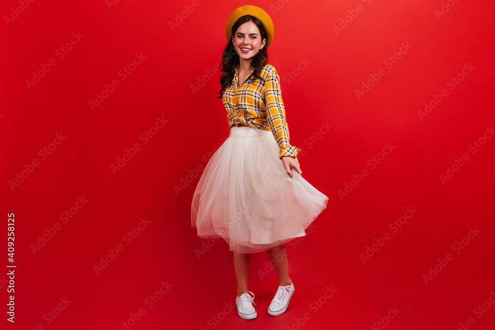 Snapshot full-length of curly dark-haired girl in bright outfit. Woman in beret and fluffy skirt is spinning on red background Snapshot full-length of curly dark-haired girl in bright outfit. Woman in beret and fluffy skirt is spinning on red background