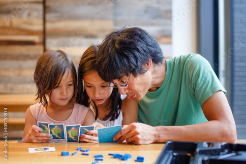 A father plays a board game with his daughters at a wooden table