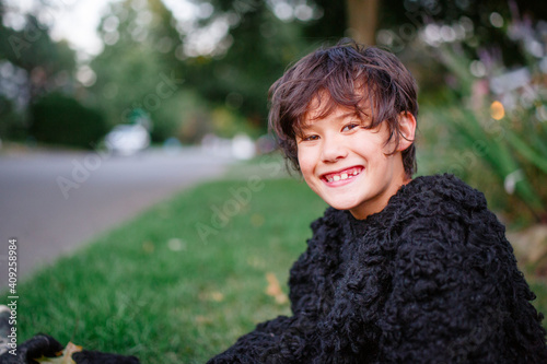 A happy boy in a gorilla suit smiles and sits in a grassy yard photo