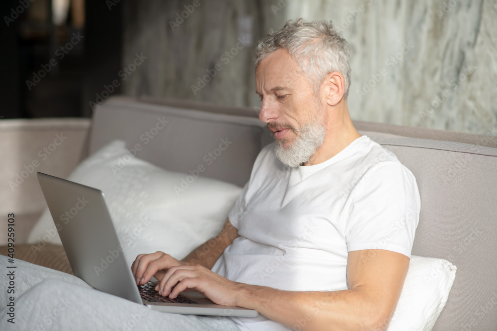 Serious man working on laptop in bed Serious man working on laptop in bed