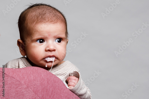 A baby boy held in his mothers arms spits up formula and stares photo