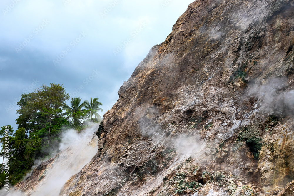 Smoking mountain rocks above green trees, volcanic island nature. Abstract mountain landscape with geyser smoke. Volcano caldera view. Canyon hiking banner template. Mountain and palm tree landscape