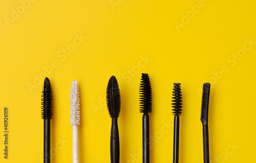 Various types of mascara wands on yellow surface