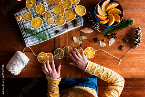 Childs hands putting together dried orange garland for Christmas