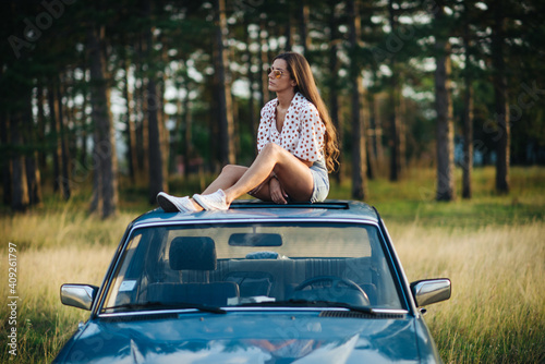 A woman sitting on the roof on a car.