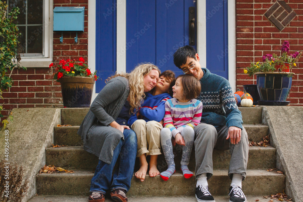 A loving family snuggle together on front stoop of home in autumn A loving family snuggle together on front stoop of home in autumn