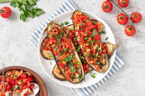 Baked eggplant with tomatoes, peppers, onions, parsley, and olive oil in a plate on a gray concrete table top view. Tasty vegetarian food Mediterranean style.