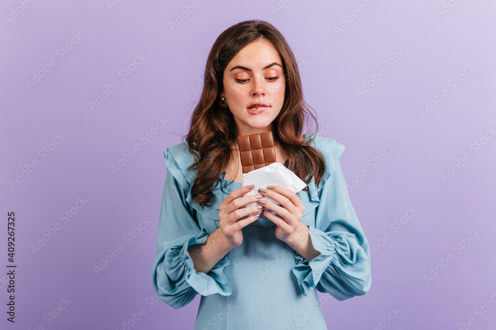 Portrait of funny brunette woman biting her lip in anticipation of tasty lunch. Girl in blue dress looks at delicious chocolate Portrait of funny brunette woman biting her lip in anticipation of tasty lunch. Girl in blue dress looks at delicious chocolate