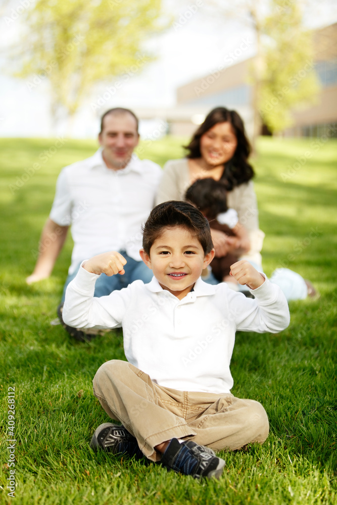 Boy flexing while sitting in front of family in grass
Boy flexing while sitting in front of family in grass