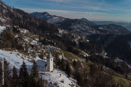Aerial drone view of Catholic church of Holy Ahacij in Kalise, Slovenia on a sunny winter day with some snow visible. Cold but warm feeling.