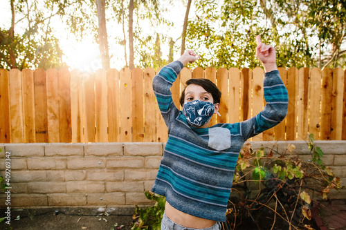 Boy Outside Wearing A Cloth Face Mask Lifts His Arms Up Exposing Belly photo