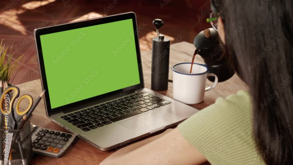 Over the shoulder shot of a business woman working in office interior on pc on desk, looking at green screen. Office person using laptop computer with laptop green screen, sitting at wooden table