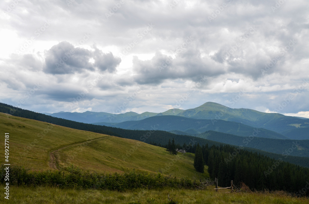 The green slope pasture with Chornohora mountain range in the background under clouds. Beautiful natural landscape in the summer time